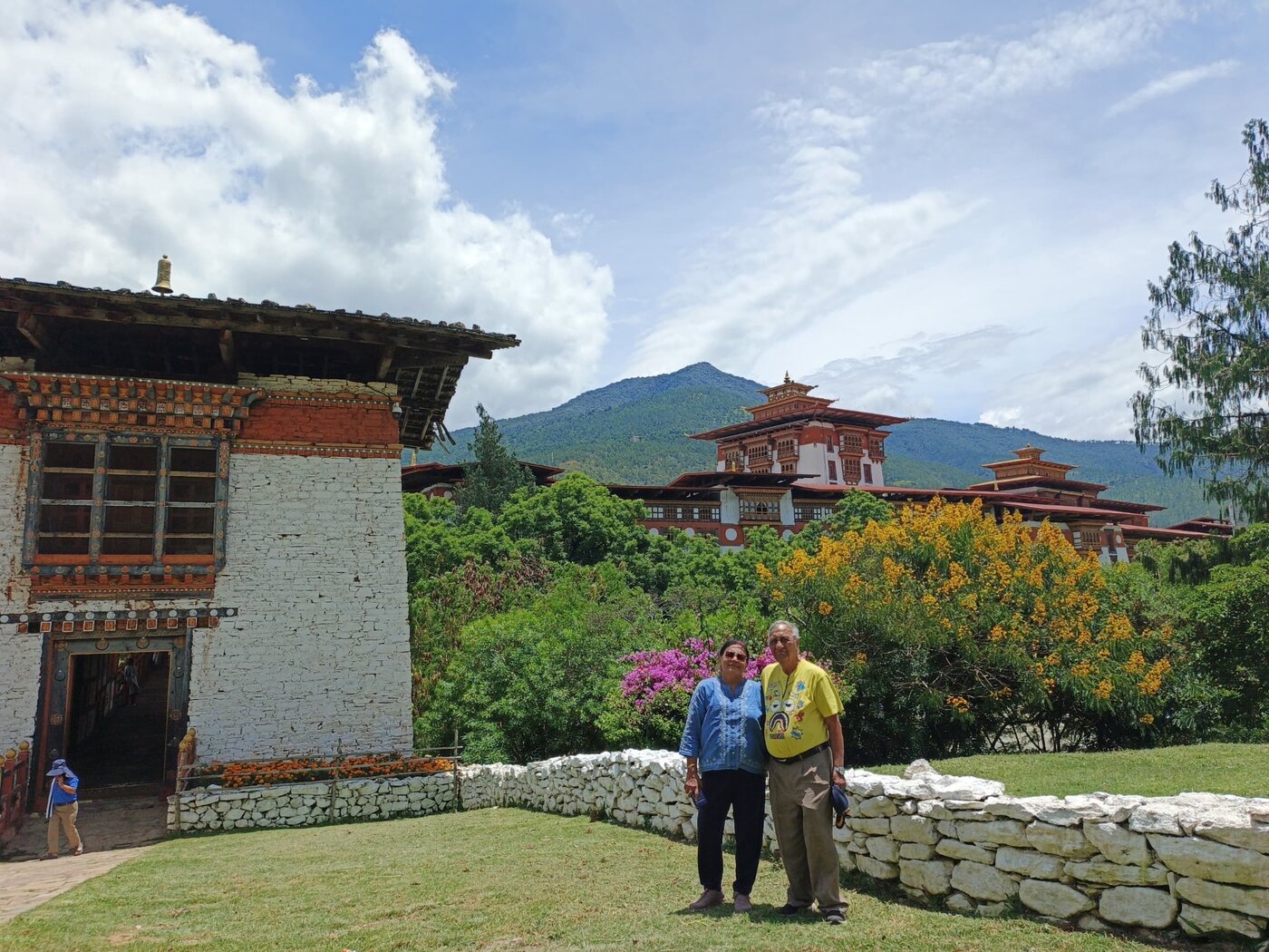 Travellers in a garden surrounded by traditional Bhutanese architecture and forested mountains